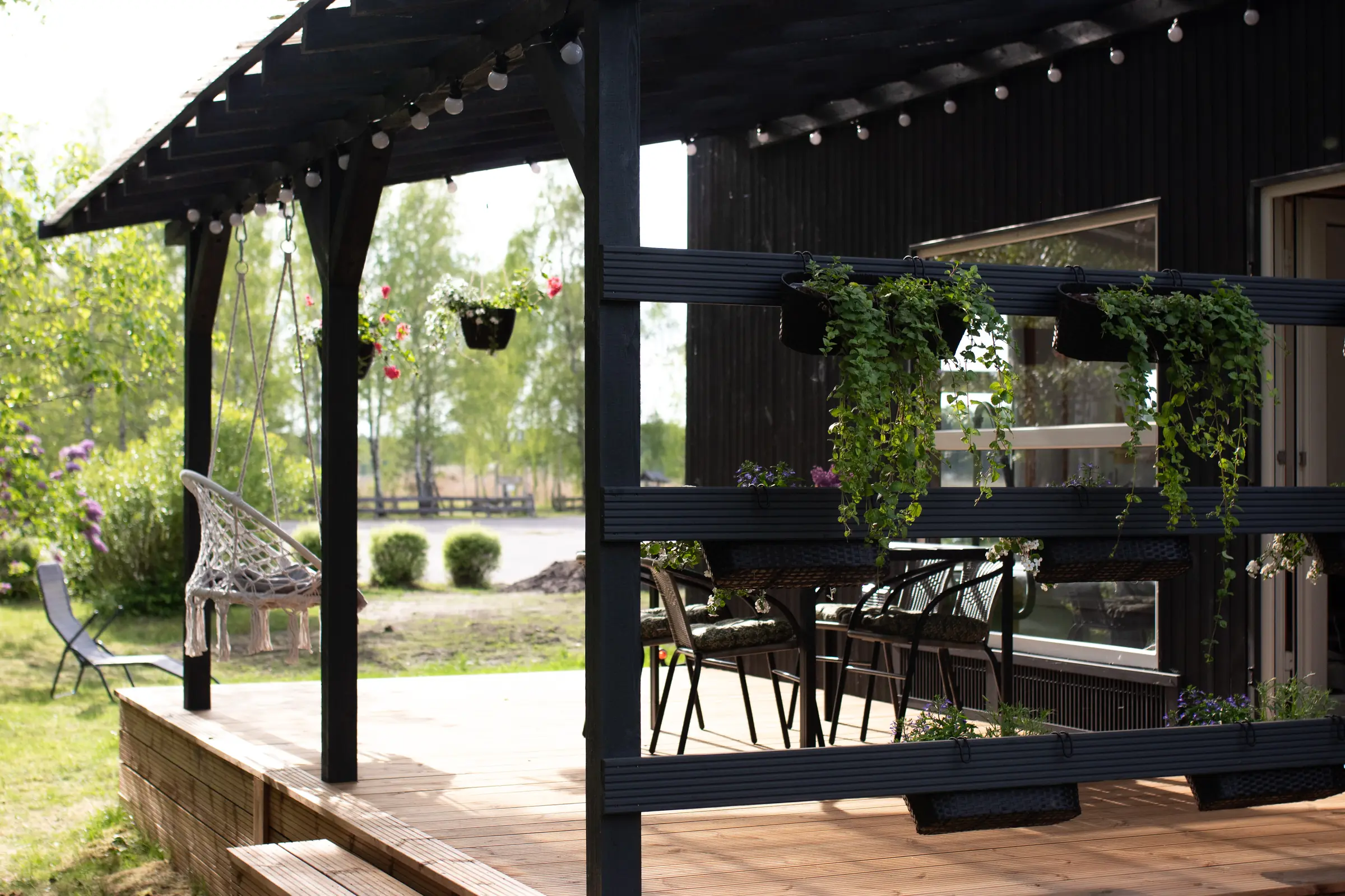 Pergola ar lampiņām pie Saulrieta, aiz tās bērzu birzs